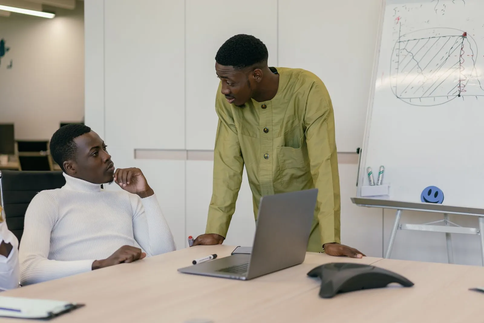Two men in a meeting room discussing terms over a laptop